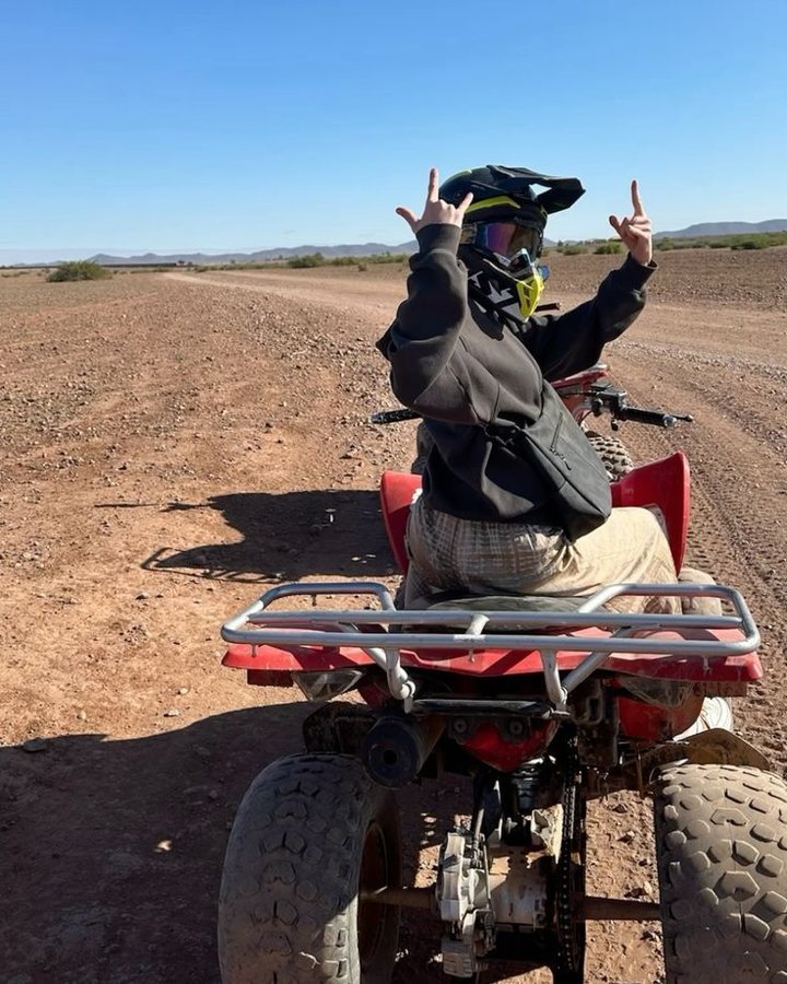 Quad Marrakech Palmeraie : pilote en casque sur un quad rouge, les mains levées, sur une piste de terre